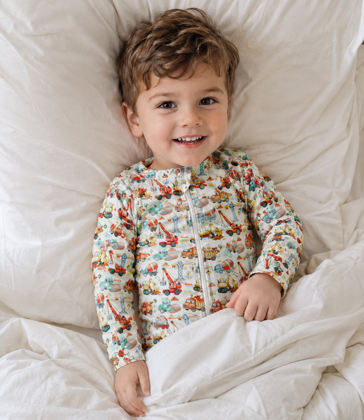 Boy in bed wearing little Acres Co construction print organic cotton growsuit or onesie. 