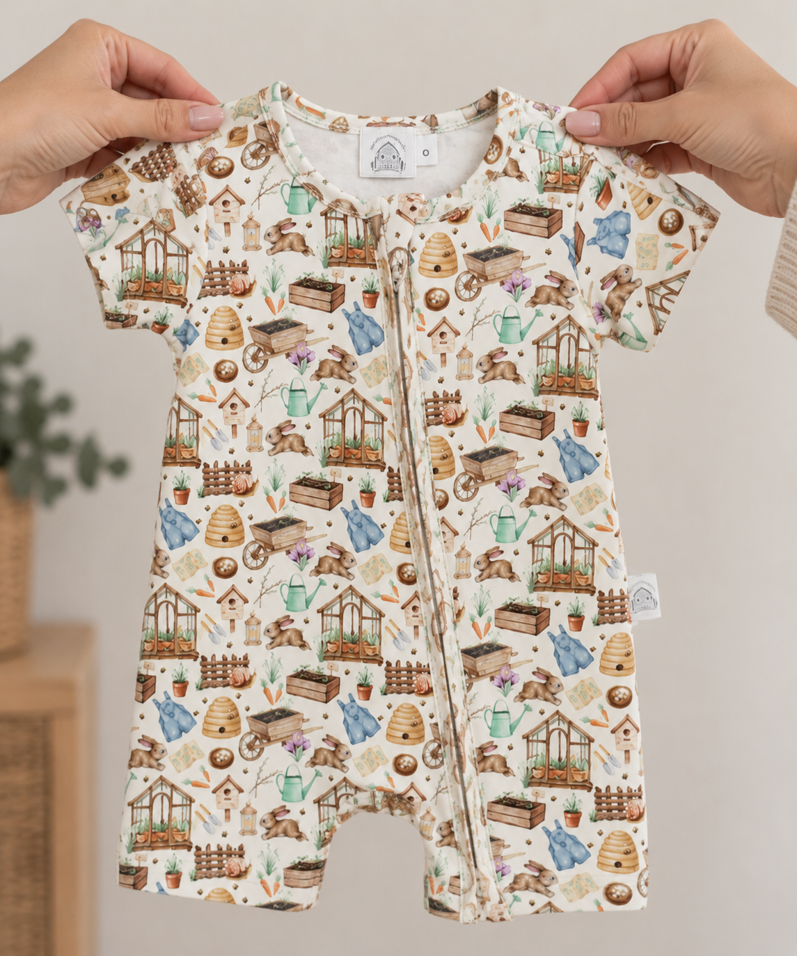 Hands holding Little Acres Co garden print baby zip-up romper in GOTS organic cotton. Australian brand