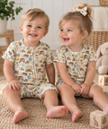 Boy and girl wearing Little Acres Co garden print organic cotton zip-up rompers